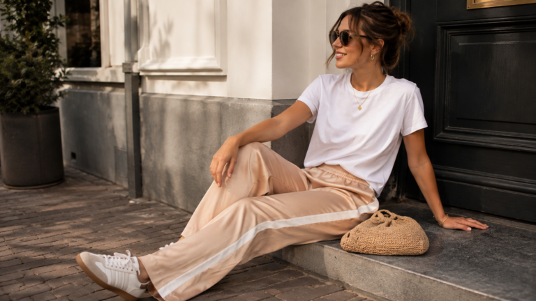 Vrouw draagt beige satijnen broek met witte contrastbies in een casual najaarsoutfit.